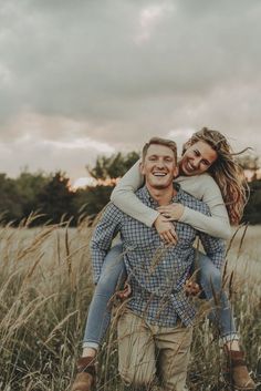 a man carrying a woman on his back through tall grass in the middle of a field