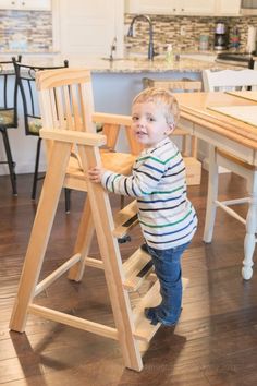 a little boy standing on top of a wooden step stool in a kitchen next to a table