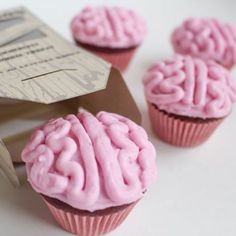 some pink cupcakes are sitting on a white table and one is shaped like a brain