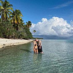 two people are standing in the water near some palm trees