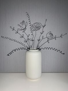 a white vase filled with flowers on top of a table next to a wallpaper