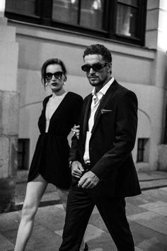 black and white photograph of man and woman walking down the street in front of a building