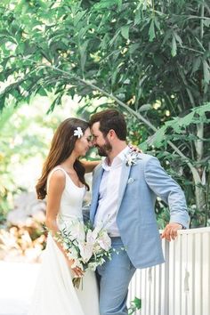 a bride and groom standing next to each other in front of a white picket fence