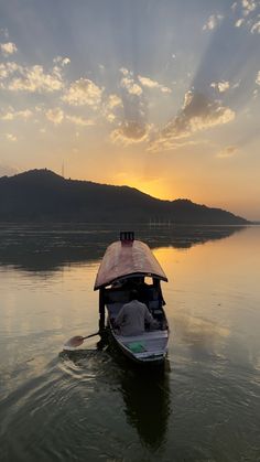 a small boat floating on top of a lake under a cloudy sky with the sun going down