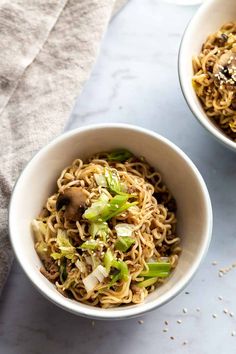 two bowls filled with noodles and vegetables on top of a white countertop next to a napkin