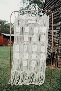 a white macrame hanging in front of a wooden structure with tags on it