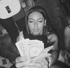 black and white photograph of woman holding stacks of money in front of her face, with other people behind her