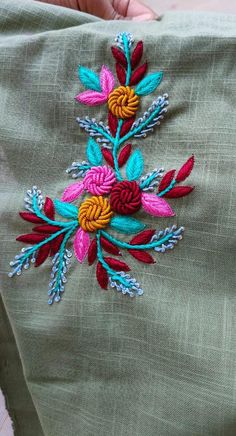 someone is stitching something on top of a piece of cloth with colorful flowers and leaves