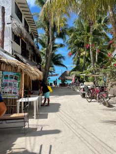 people are standing on the beach near some buildings and palm trees, with bicycles parked in front of them