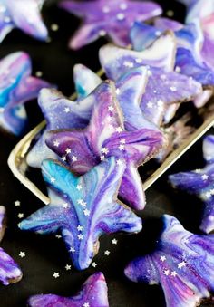 purple and blue decorated cookies sitting on top of a black plate with sprinkles