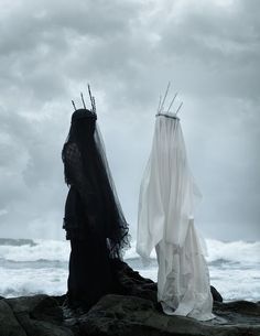 two people dressed in black and white standing on rocks near the ocean