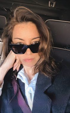 a woman wearing sunglasses sitting in the back of a car with her hand on her face