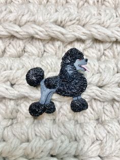 a black poodle sitting on top of a white crochet blanket with it's tongue sticking out