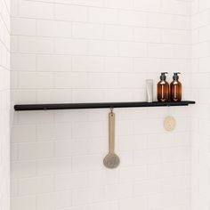 two bottles and a spatula on a shelf in a white tiled bathroom with black grouting