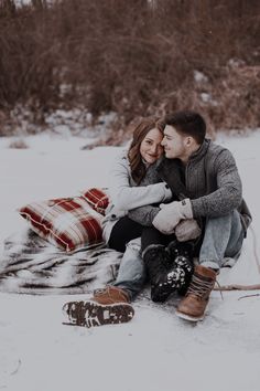 a man and woman sitting on top of a snow covered ground next to each other