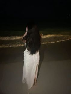 a woman standing on top of a beach next to the ocean under a dark sky