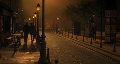 people walking down the street at night in an old city with lights on and fog