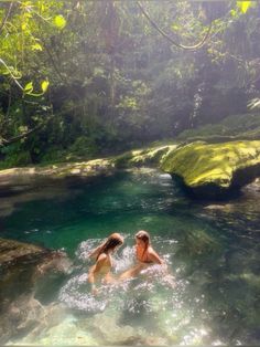 two people swimming in a river surrounded by trees