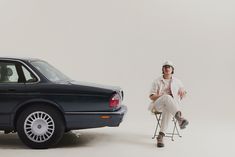 a man sitting on a chair next to a black car