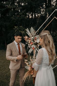 a man in a suit and tie standing next to a woman holding a bouquet with flowers