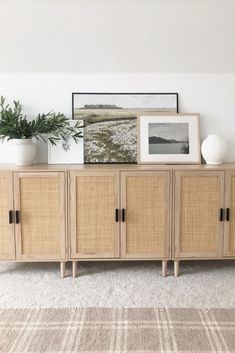 a sideboard with some plants on top of it and pictures above the drawers in front of it