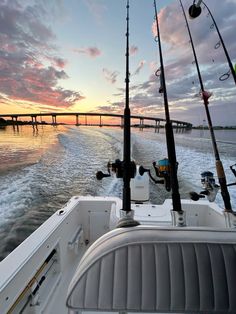 two fishing rods on the back of a boat in the water at sunset with a bridge in the background