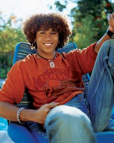 a young man sitting in a blue chair with his hand up to the camera and smiling