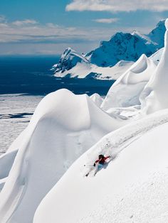 a person skiing down the side of a snow covered mountain with mountains in the background