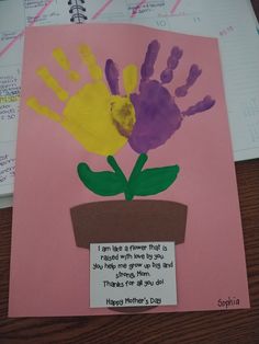 a child's handprint flower pot on a desk with a note attached to it