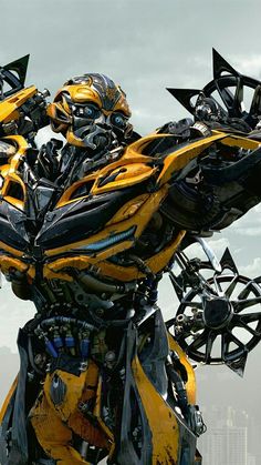 a large yellow and black robot standing in front of a cloudy sky with buildings behind it