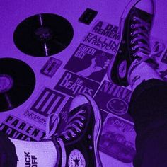 a person's feet in black and white sneakers on top of purple paper with various records