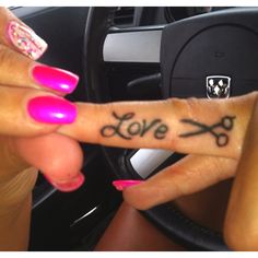 a woman with pink nails is holding up her hand that has scissors and the word love written on it