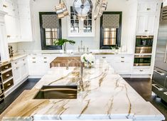 a large kitchen with marble counter tops and white cabinets, along with an island in the middle