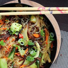 a bowl filled with noodles, vegetables and chopsticks on top of a table