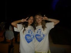 two young women standing next to each other with their hands in the air while making heart signs