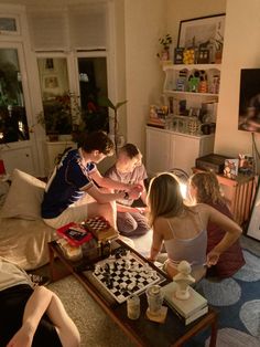 four people sitting on a couch in a living room, playing chess and drinking coffee