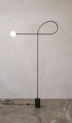 a black floor lamp with a round light bulb on it's side and a cord attached to the base