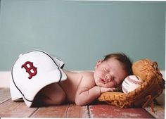 a baby laying on top of a wooden floor next to a baseball glove and ball