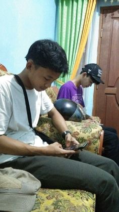 two young men sitting on couches looking at their cell phones