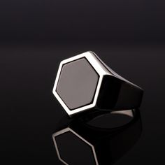 a black and white ring with an octagonal design on the front, sitting on a reflective surface