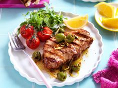 a white plate topped with meat and veggies next to a fork on a blue tiled table