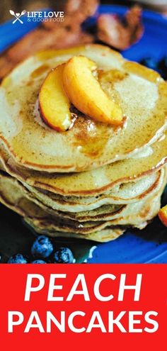 a stack of pancakes on a blue plate topped with peaches and syrup next to sliced fruit