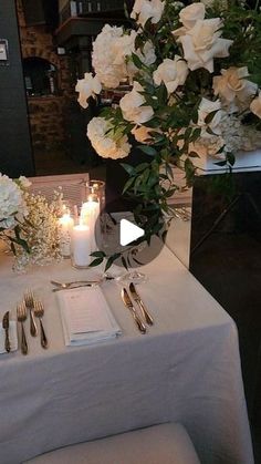 the table is set with silverware and white flowers in vases, candles and menu cards