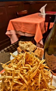 french fries and bread on a plate with a bottle of wine in the back ground