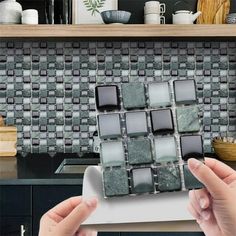 two hands are holding a tablet in front of a kitchen counter with tiles on it