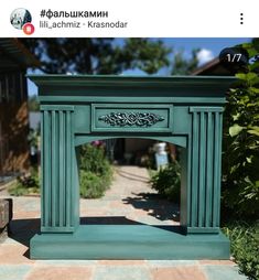 a green fireplace with an ornate design on the top and bottom part, in front of some bushes