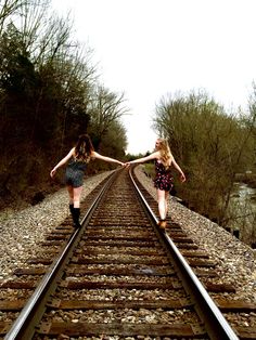 two young women are walking down the railroad tracks holding hands and looking at each other