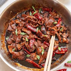 a pan filled with meat and vegetables on top of a table next to chopsticks