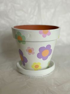 a flower pot sitting on top of a saucer with an orange bottom and purple flowers