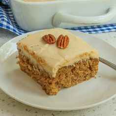 a piece of carrot cake with frosting and pecans on top, sitting on a white plate